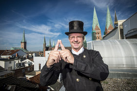 Schornsteinfeger Jens Karwinski macht das Sieben-Türme-Symbol mit seinen Zeigefingern. Die Finger zeigen eine Turmspitze.